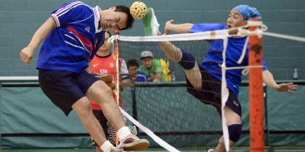 Player in foreground is shooting ball by foot and head in acrobatic way.